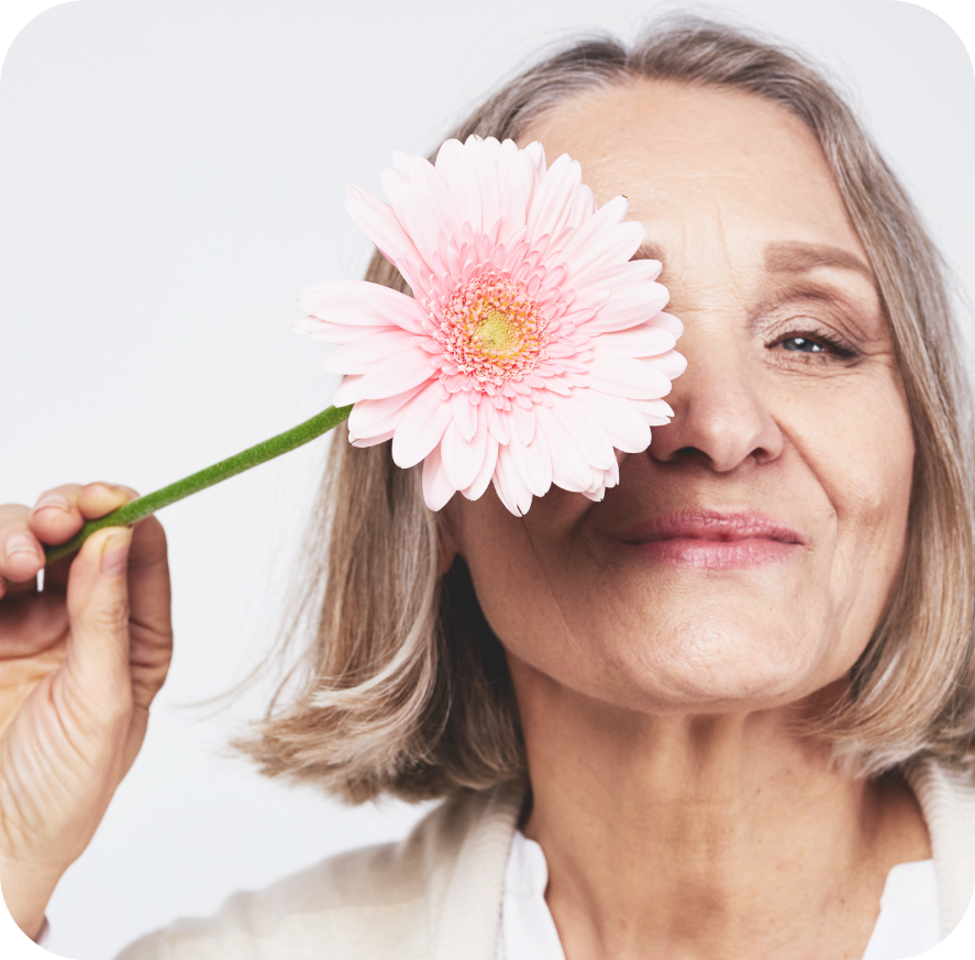 Visage femme âgée souriante masquée partiellement par une grosse fleur rose pâle