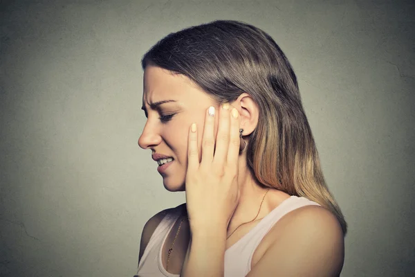 Visage d'une jeune femme de profil, la main sur l'oreille et grimaçant de douleur. Sophrologie et hypnose face à la douleur
